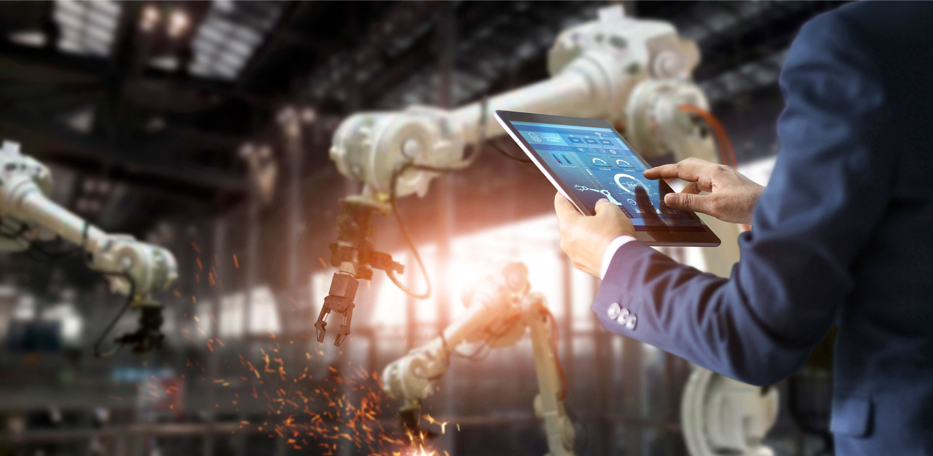A person wearing a blue suit (only hands and forearms are visible) is controlling robots via a tablet.