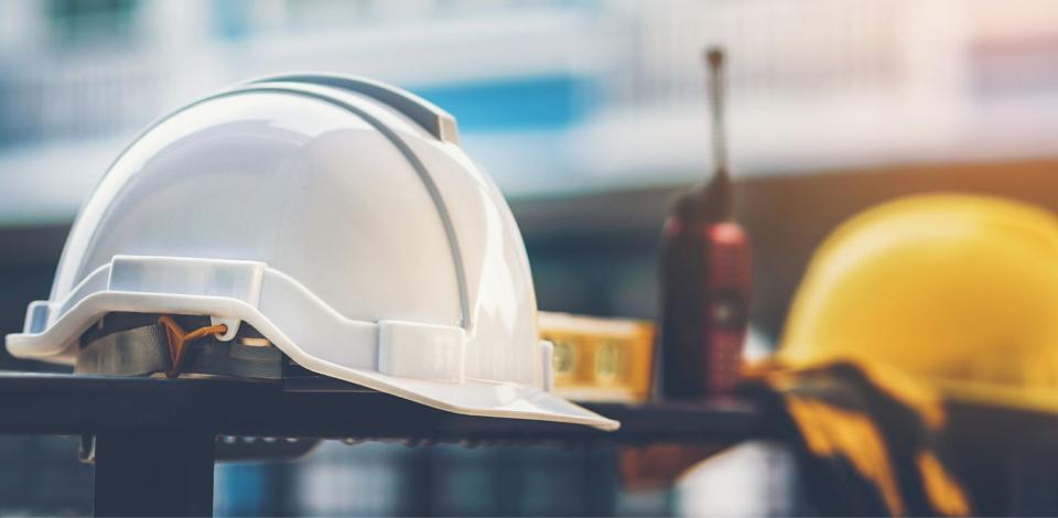 White and yellow helmet with construction water,gloves and radio that are placed on steel house fence.