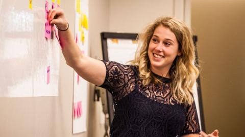 Female at white board adjusting process mapping sticky notes.