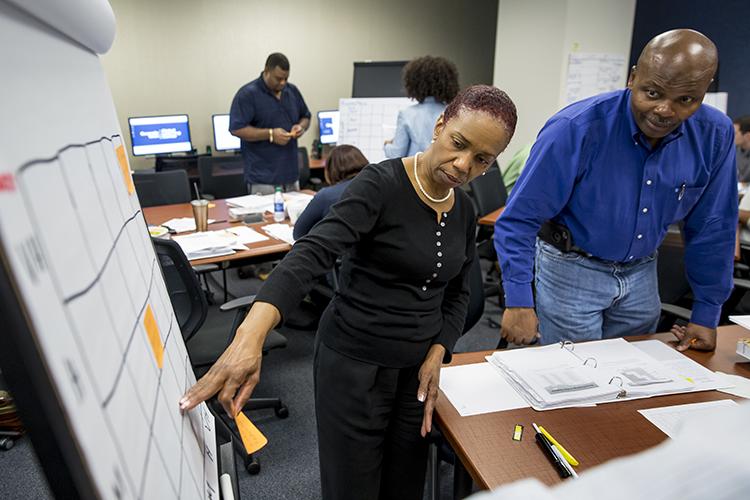 Male and female GTPE learners work on a project at a flip chart in the classroom.