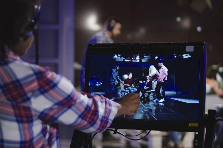 Film producer in headset controlling process of shooting TV in front of computer screen